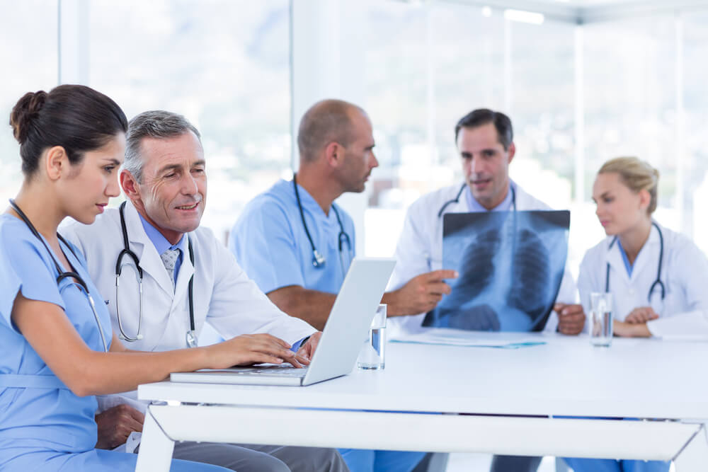 Doctors using computer whiles theirs colleagues looking at Xray in medical office 